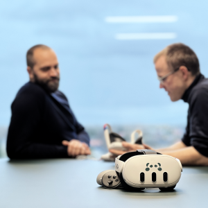 Kristian_And_Franz_With_VR_Headset_1200x1200 Two guys sitting at a table with a VR headset in front of them